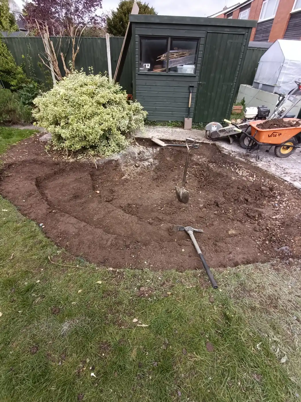 Pond excavation in progress with tools and wheelbarrow